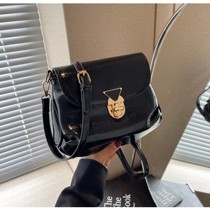 Détail du sac sous l'aisselle en cuir verni noir avec fermoir tournant doré et fini brillant