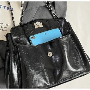 Macro view of black glossy tote bag showing chain strap and tablet inside pocket
