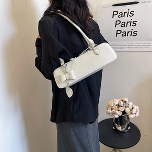 Détail du sac baguette blanc avec ornement de nœud et pendentif cœur en chaîne métal