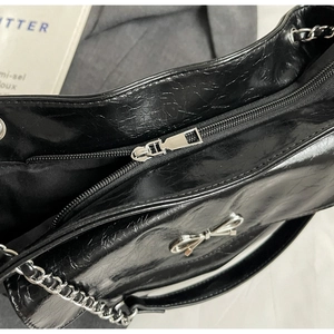Close-up detail of black crinkled patent leather tote with silver bow and metal zipper