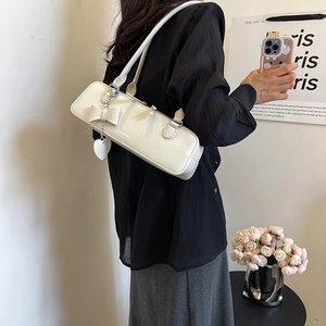 Sac sous le bras en cuir verni beige avec nœud et breloque cœur porté par un mannequin