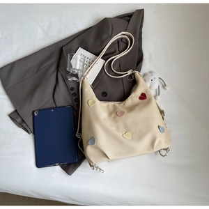 Dettaglio della borsa tote in tela bianco sporco con toppe a cuore colorate e catena argento