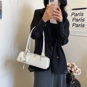 Détail d'un sac à bandoulière crème minimaliste avec pendentif nœud décoratif et fini lisse