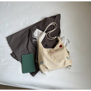 Dettaglio borsa tote in tela beige con toppe a cuore colorate e decorazione a catena