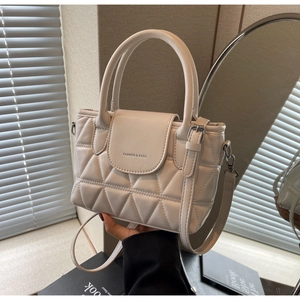 Close-up of cream quilted bucket bag with double handles and fashion text detail