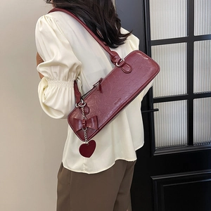 Détail du sac baguette en cuir bordeaux avec pendentif coeur et nœud sur un mannequin