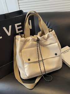 Sac cabas beige en toile avec cordon de serrage et bandoulière sur un canapé en cuir