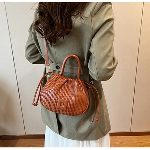 Détail d'un sac seau plissé marron porté avec un blazer vert et une jupe blanche
