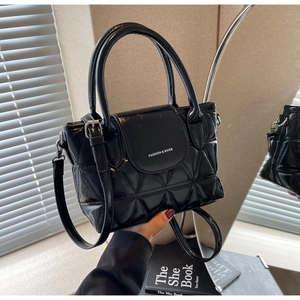 Close-up of black glossy quilted bucket bag with double handles and mirror reflection