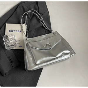 Close-up of silver tote bag with metal bow buckle and chain strap on grey blazer
