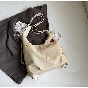Dettaglio borsa tote in tela beige con toppe a cuore colorate e catena in metallo