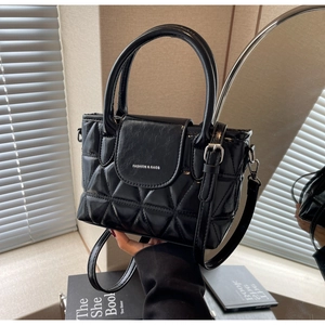 Detail of black quilted bucket bag with silver logo and dual handles on a windowsill