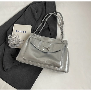 Detail of silver metallic tote bag featuring a chic metal bow and chain shoulder strap