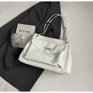 Close-up of white tote bag featuring a silver bow buckle and elegant metal chain strap