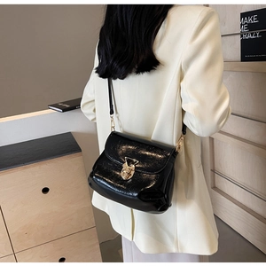 Détail du sac en cuir verni noir avec une boucle métallique triangulaire dorée distinctive