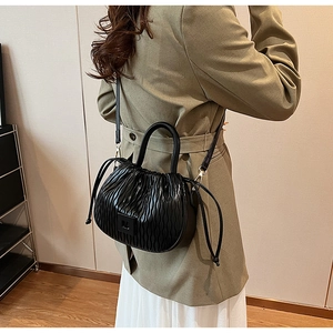 Détail d'un sac nuage noir plissé avec cordon, porté par un mannequin en blazer vert