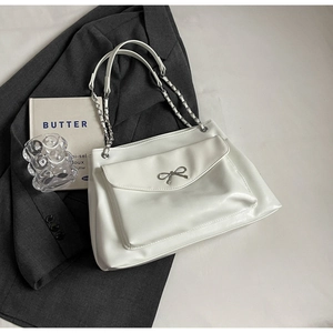 Close-up of stylish white tote bag featuring a silver bow detail and metal chain strap