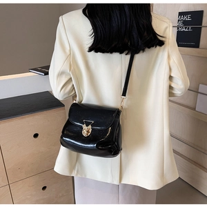 Gros plan sur un sac bandoulière en cuir verni noir avec fermoir tournant en métal doré