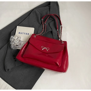 Detail of red patent leather tote bag with silver bow ornament and chain strap