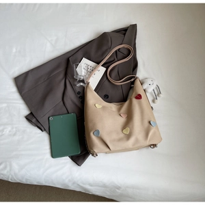 Dettaglio borsa a mezzaluna beige con toppe a cuore colorate e tracolla sottile
