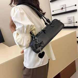 Détail du sac baguette noir brillant avec nœud et pendentif en forme de cœur argenté