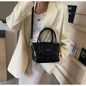 Quilted black bucket bag with silver hardware held by model against wooden shelf
