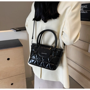Detail of black quilted bucket bag with polished metal plaque and round top handle