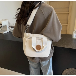 Sac fourre-tout blanc en toile avec large bandoulière et patch logo dans un café