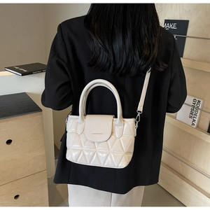Quilted off-white handbag shown from a side view on a model wearing a black blazer