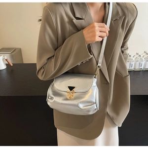 Détail du sac à bandoulière argenté plissé avec fermoir doré porté par un mannequin