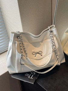 Chic white tote bag with silver bow charm and chain strap on a modern background