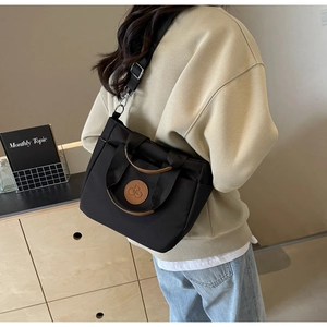 Détail d'un sac cabas en toile noir avec anses en cuir marron porté par un mannequin