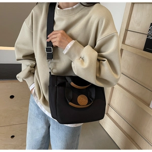 Détail du cabas en toile noire avec patch logo en cuir marron et bandoulière amovible