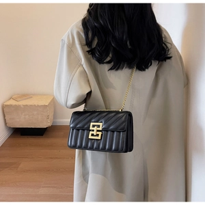 Détail d'un sac bandoulière matelassé noir avec chaîne dorée et boucle en métal sur modèle