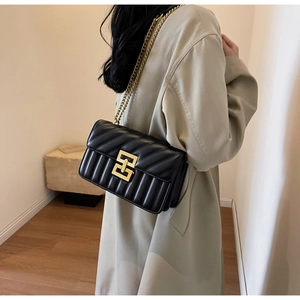 Sac bandoulière en cuir matelassé noir avec chaîne dorée porté par un mannequin
