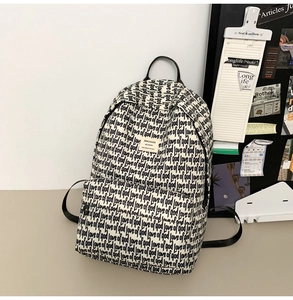 Detail view of cream canvas backpack with black lettering and durable shoulder straps