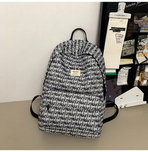 Detail of high-capacity black backpack with all-over white typography and brand patch