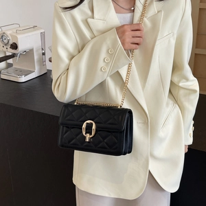 Detail of black quilted crossbody bag with gold chain strap worn with white suit