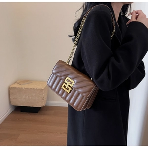 Détail du sac à bandoulière matelassé marron avec chaîne dorée sur manteau noir