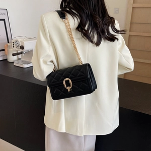 Close-up of black quilted crossbody bag with gold chain strap worn with white blazer