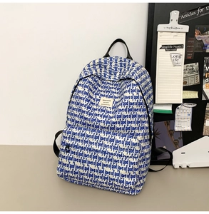 Detailed close-up of a white canvas backpack with blue lettering and front zipper pocket