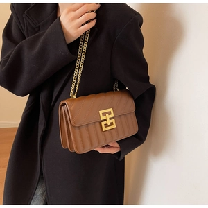 Gros plan du sac matelassé marron avec chaîne dorée porté sur un manteau noir