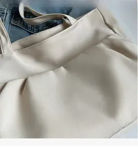 Detail of light beige tote bag with pleated side design and soft textured fabric