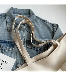 Close-up of beige canvas tote bag showing wide handle strap and metal zipper closure