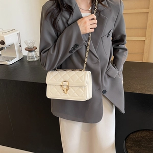 Close-up of cream quilted crossbody bag with gold U-lock and metal chain on a model
