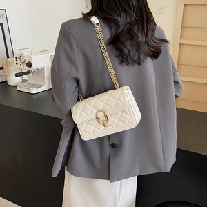 Detail of white quilted crossbody bag with gold chain strap worn with grey blazer