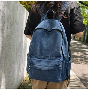 Outdoor street view of a woman wearing a blue washed denim backpack with multiple pockets