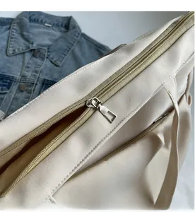 Detail shot of smooth silver metal zipper on cream-colored tote bag with denim background