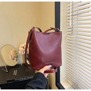 Dettaglio borsa a secchiello bordeaux con logo minimalista e tracolla regolabile