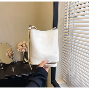 Dettaglio della borsa a secchiello in pelle crema con logo impresso e tracolla regolabile